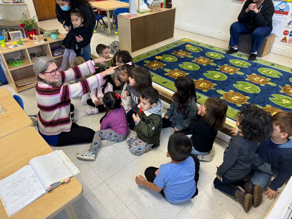 Image of happy teachers and kids sitting on the floor